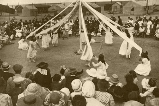 Historical community gathering with children dancing around a maypole.