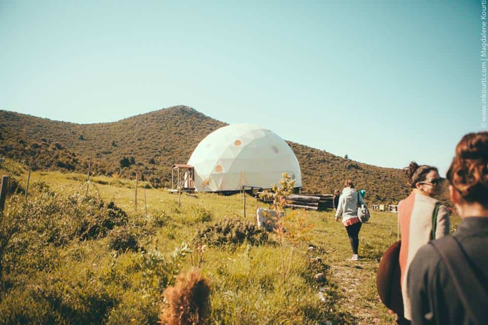 People visiting a geodesic dome in a scenic rural landscape.