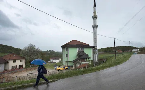 Person walking with umbrella near a mosque in a rural village setting.