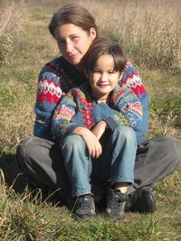 Woman and child sitting outdoors in a grassy field, smiling at the camera.