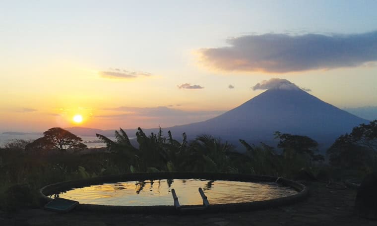 Scenic view of a volcano at sunset with a water feature in the foreground.