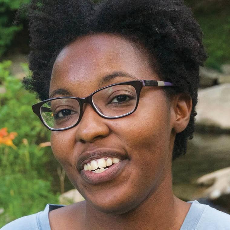 Portrait of a smiling Black woman with glasses outdoors in nature.