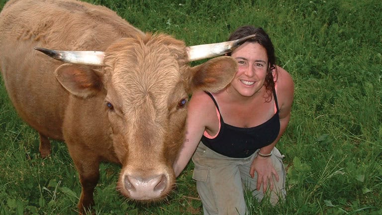 Woman smiling with a cow in a green field at Earthaven Ecovillage.
