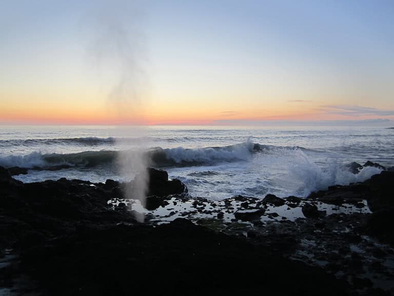 Ocean waves crashing against rocks at sunset with steam rising from the water.