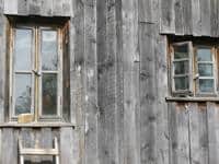 Weathered wooden building with two old windows, rustic and aged appearance.
