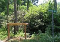 Wooden archway over a dirt path in a lush green forest setting.