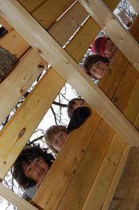 Children playing inside a wooden treehouse at a community gathering.