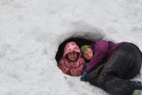 Child playing in the snow wearing pink and purple winter clothing.