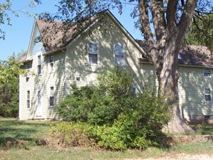 Historic green house with large trees and lush bushes in front.