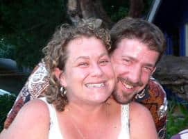 Smiling woman with curly hair and a man with a beard outdoors.
