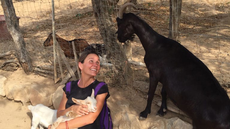 Woman with goats at a farm, smiling and petting a white goat.