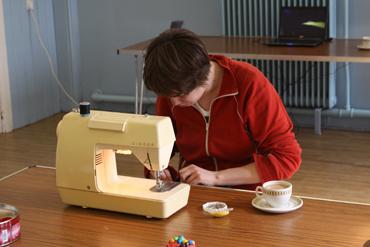 Person sewing with a vintage sewing machine at a wooden table.