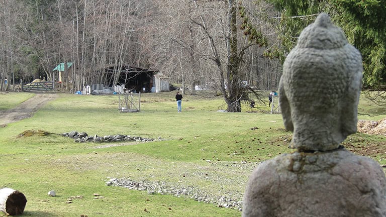 Stone sculpture overlooking a grassy community area with trees and people.