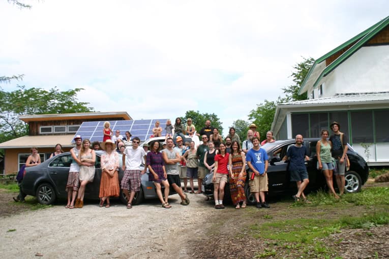 Community gathering outside eco-friendly buildings with solar panels and cars.