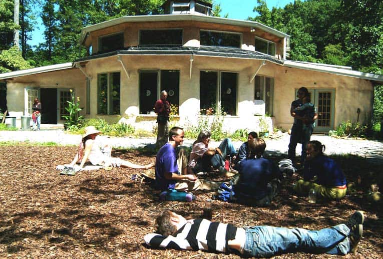 Community gathering outside a round eco-friendly building in a forest setting.