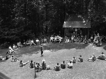 Community gathering in a grassy outdoor space with trees and a small building.