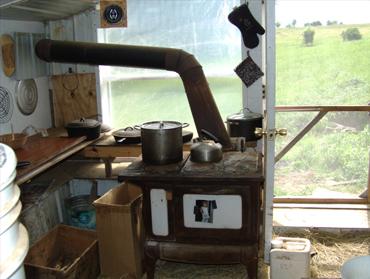 Rustic wood stove with chimney pipe in a rural home setting.