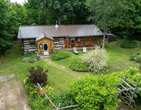 Rustic log cabin with garden and outdoor seating in a lush green setting.