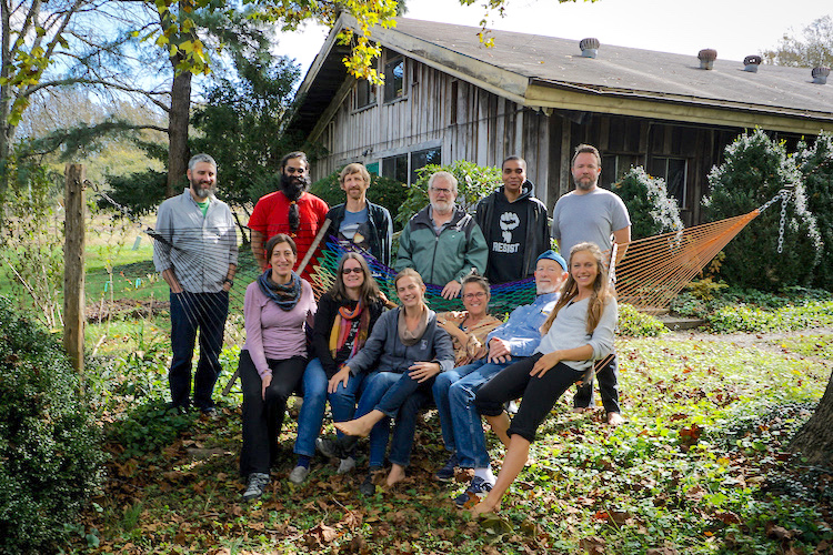 Group of diverse people in a community garden with a rustic barn in the background.