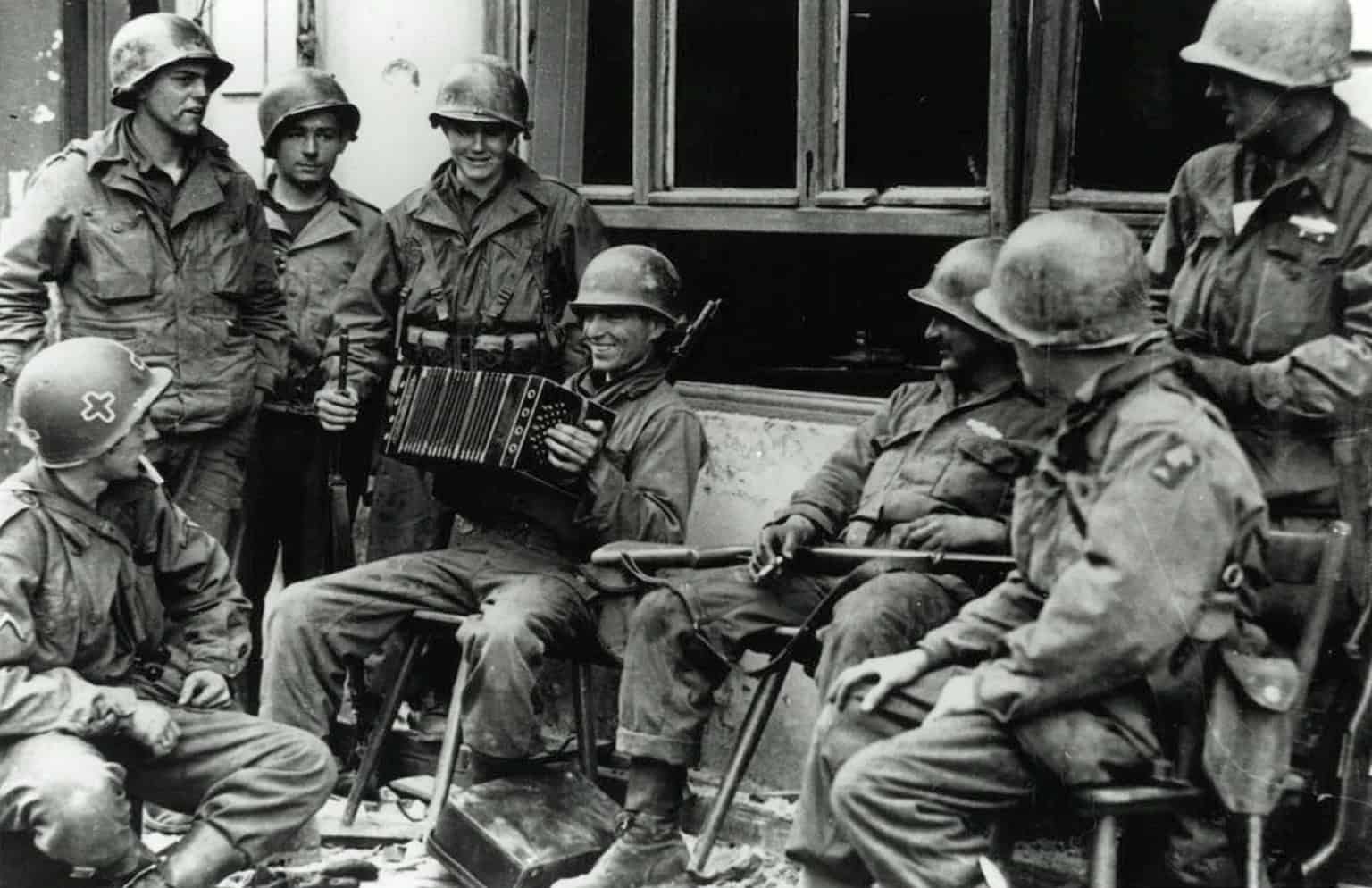 Military soldiers gathered around a soldier playing an accordion during WWII.