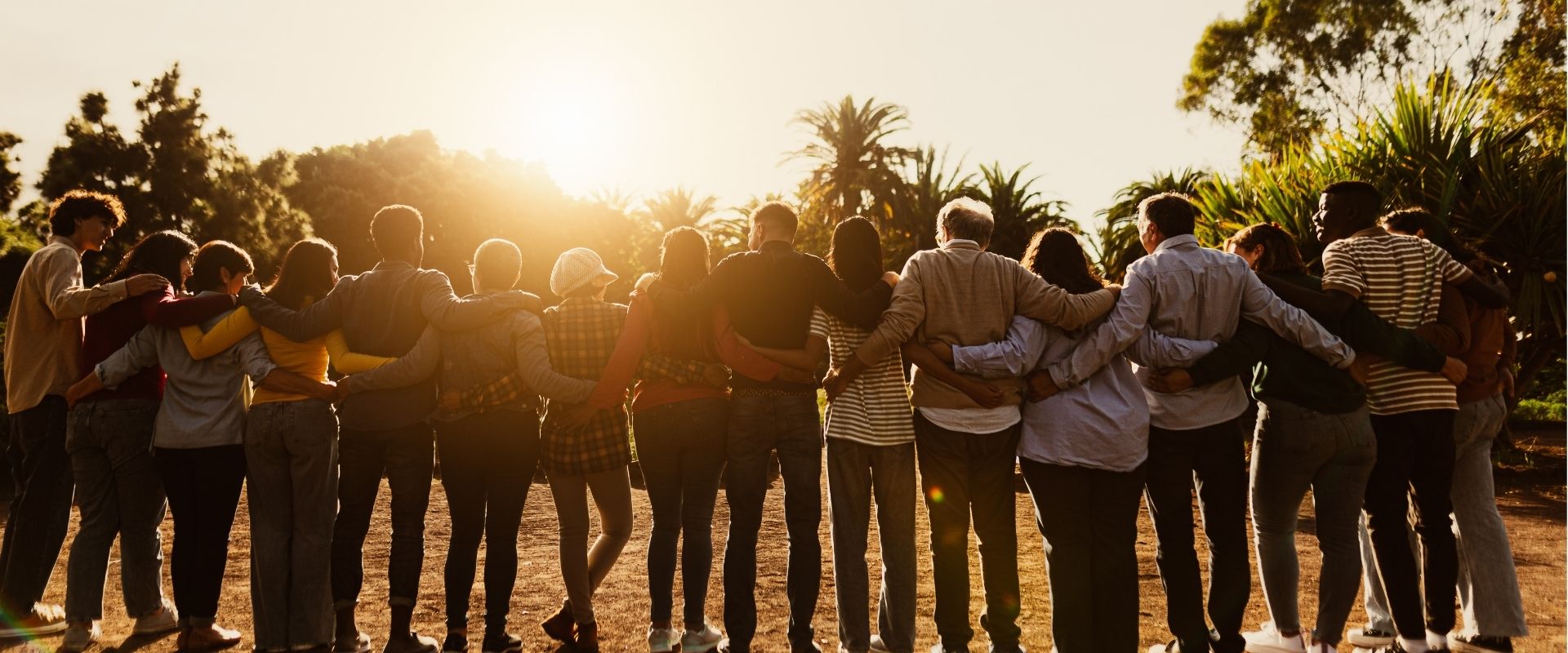 Diverse group of people standing together outdoors at sunset, holding hands.
