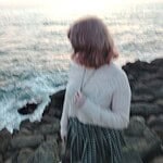 Person standing on rocky coast near ocean at sunset for community living.