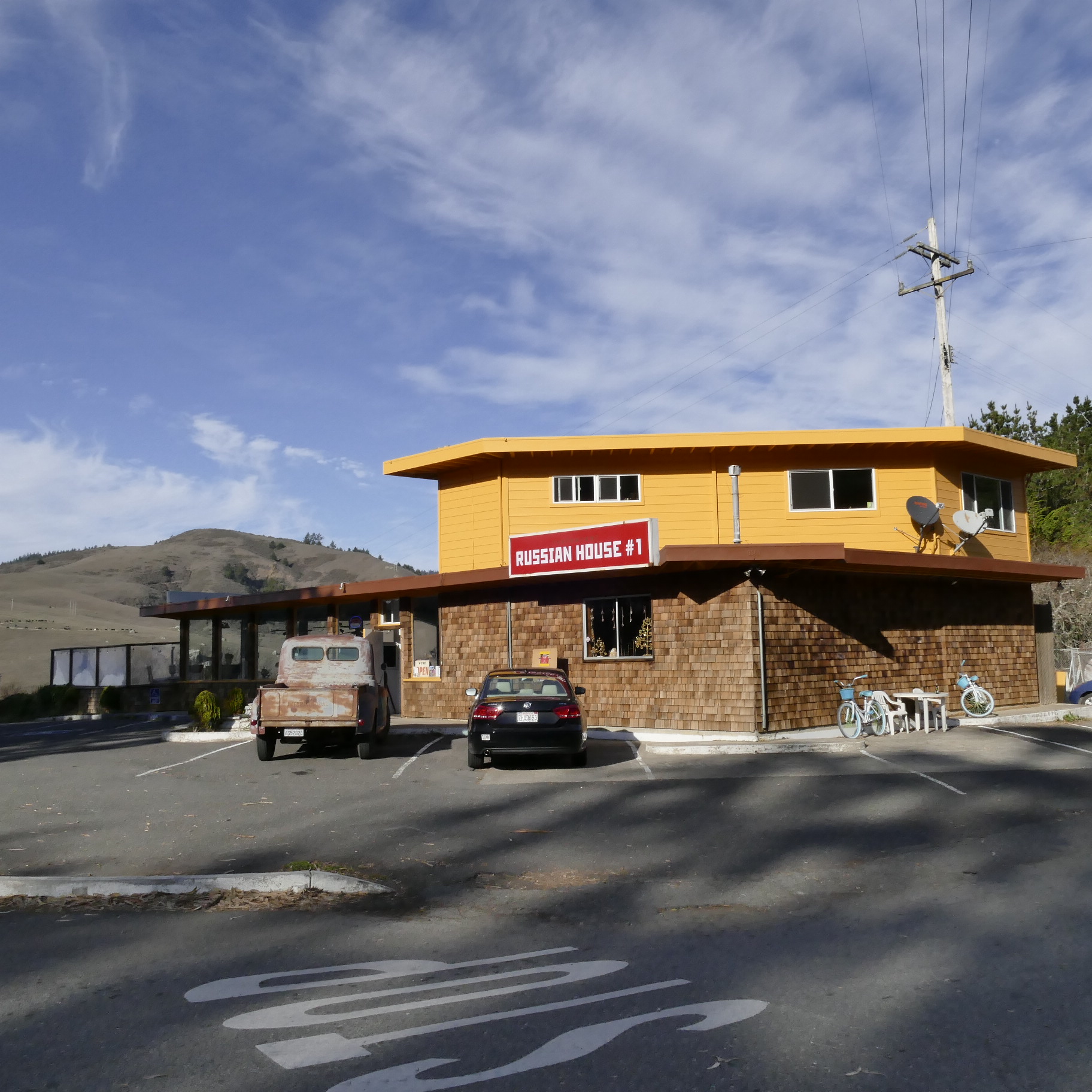 Colorful Russian-style house with parking lot and mountains in background.