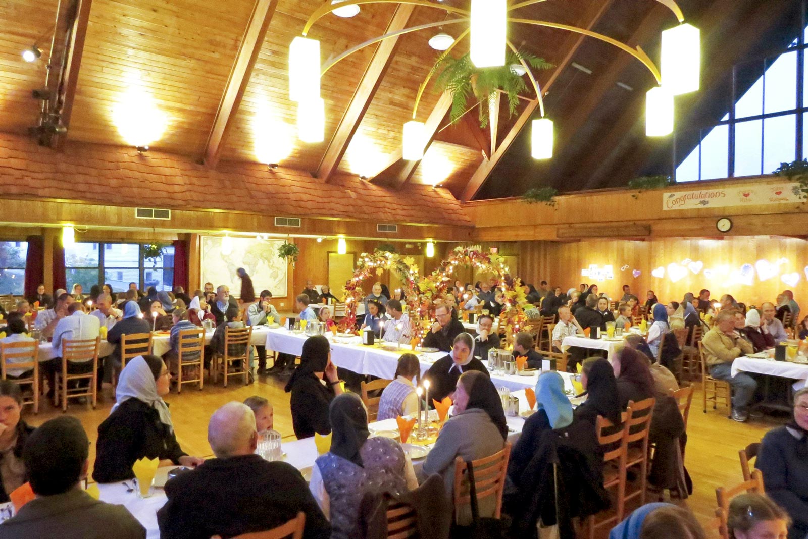 Large indoor community event with people dining and socializing in a wooden hall.