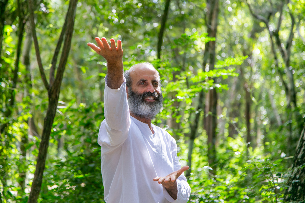 Man with white clothing meditating in lush green forest environment.