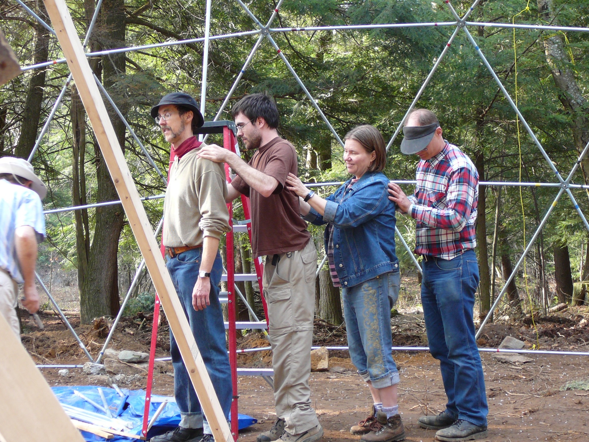 Group of people constructing a geodesic dome in a forest setting.