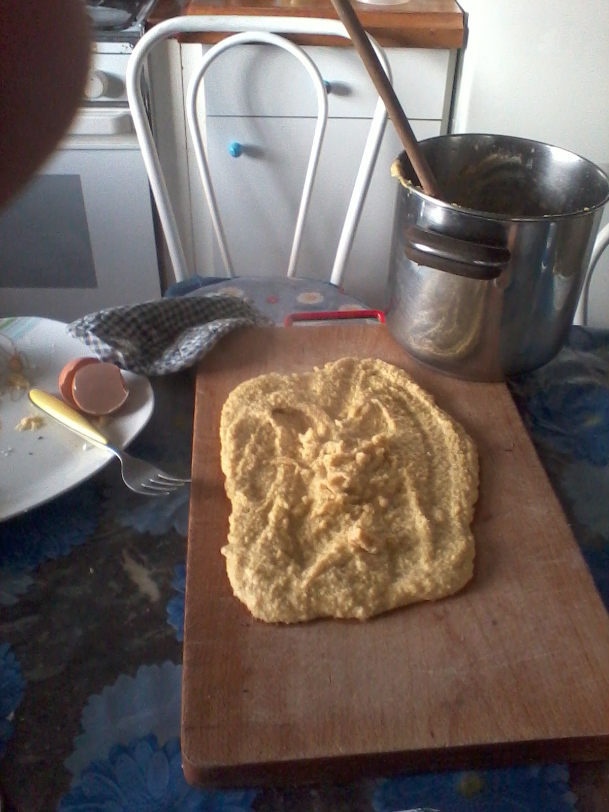 Freshly baked bread on a wooden cutting board with a metal pot nearby.