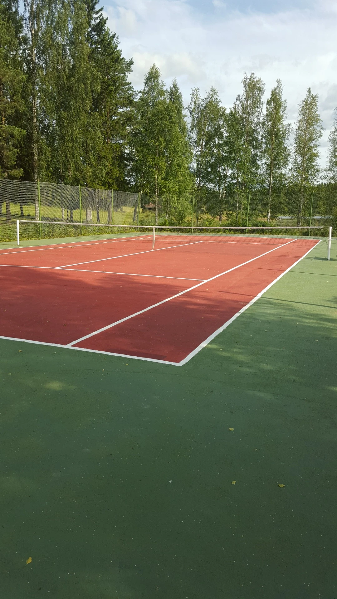 Outdoor tennis court surrounded by trees in Finland for community recreation.