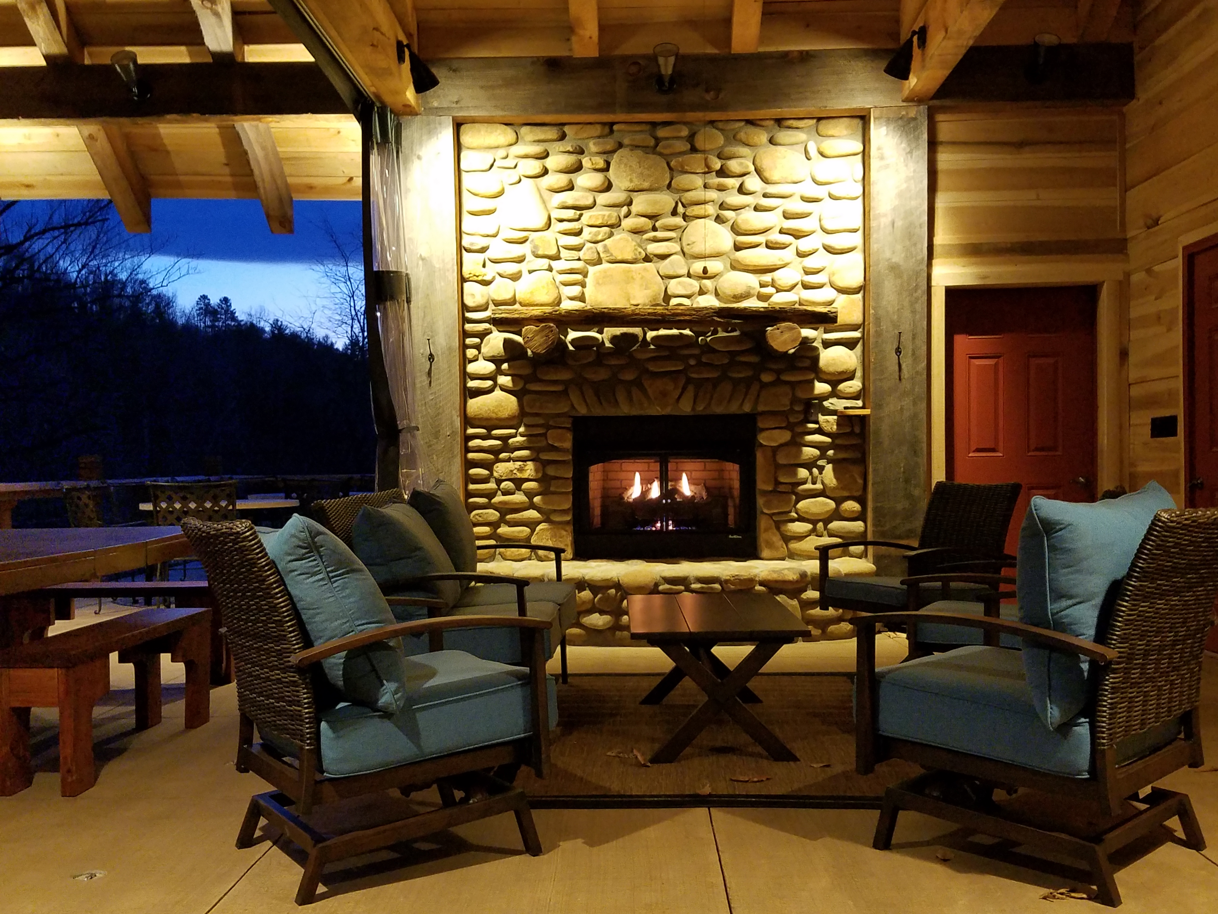 Warm living room with stone fireplace and outdoor view at dusk.