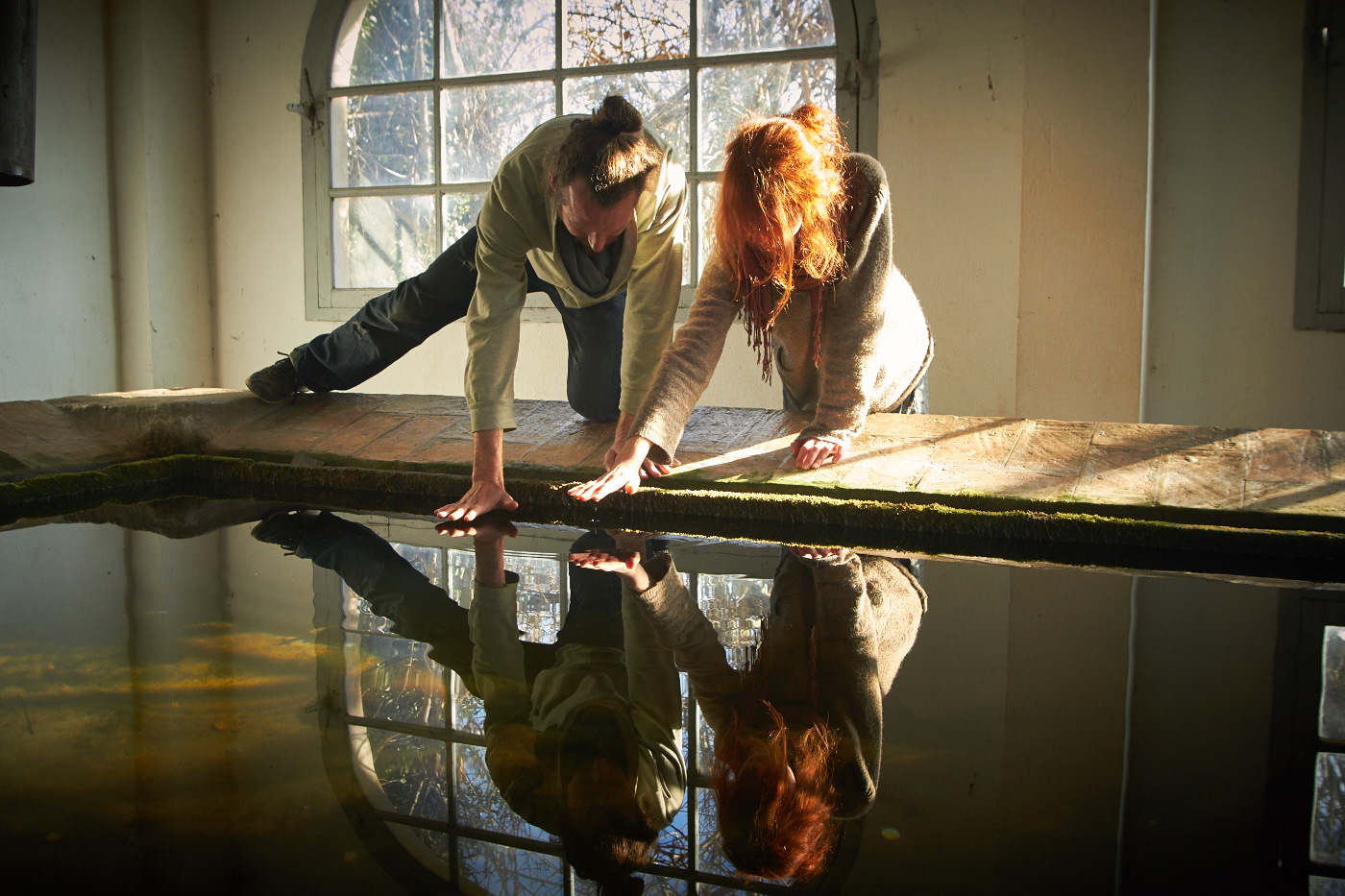 Two women examining water level in an indoor environment with large windows.
