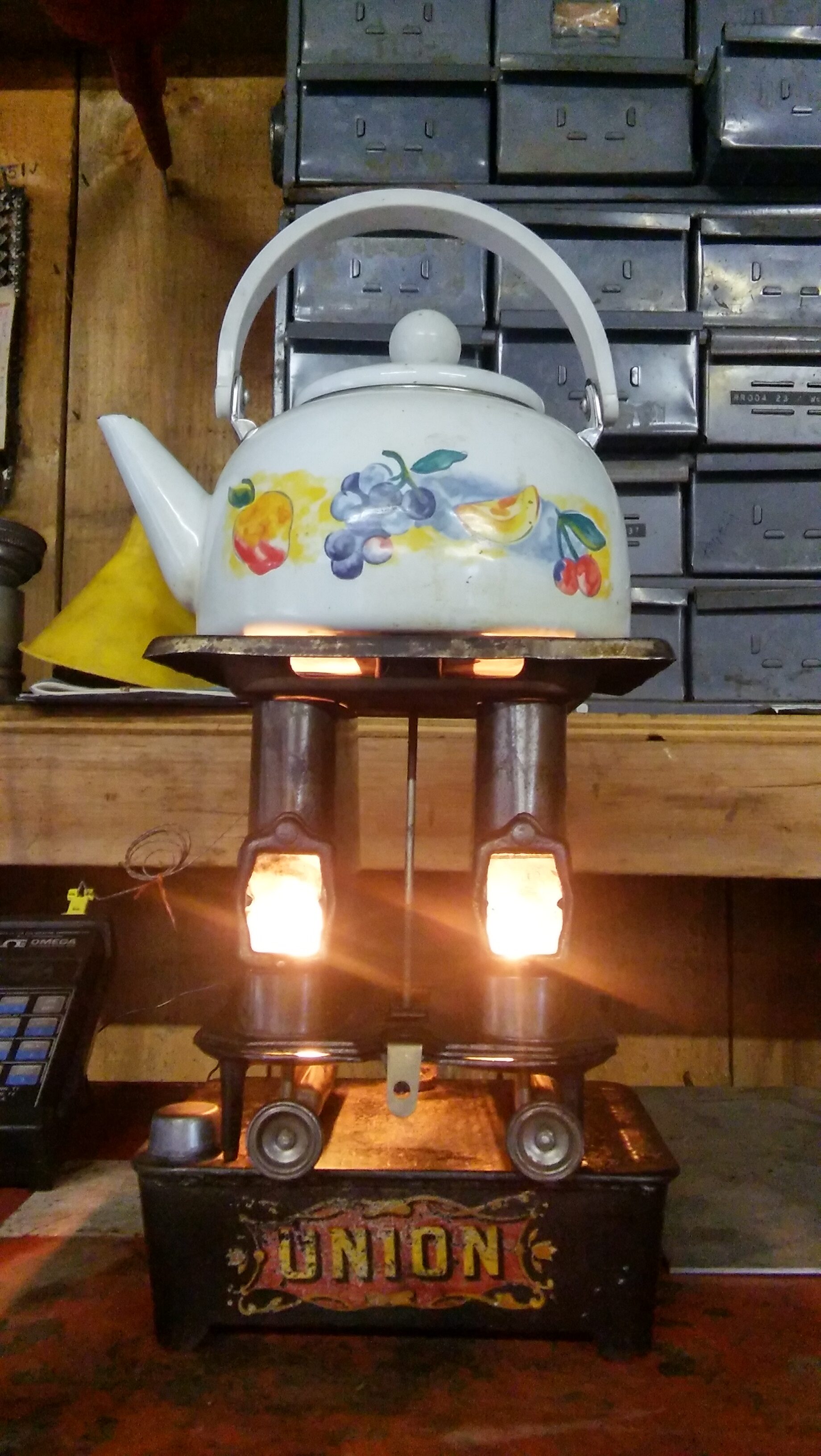 Decorative teapot on a vintage stove with lights and storage boxes.