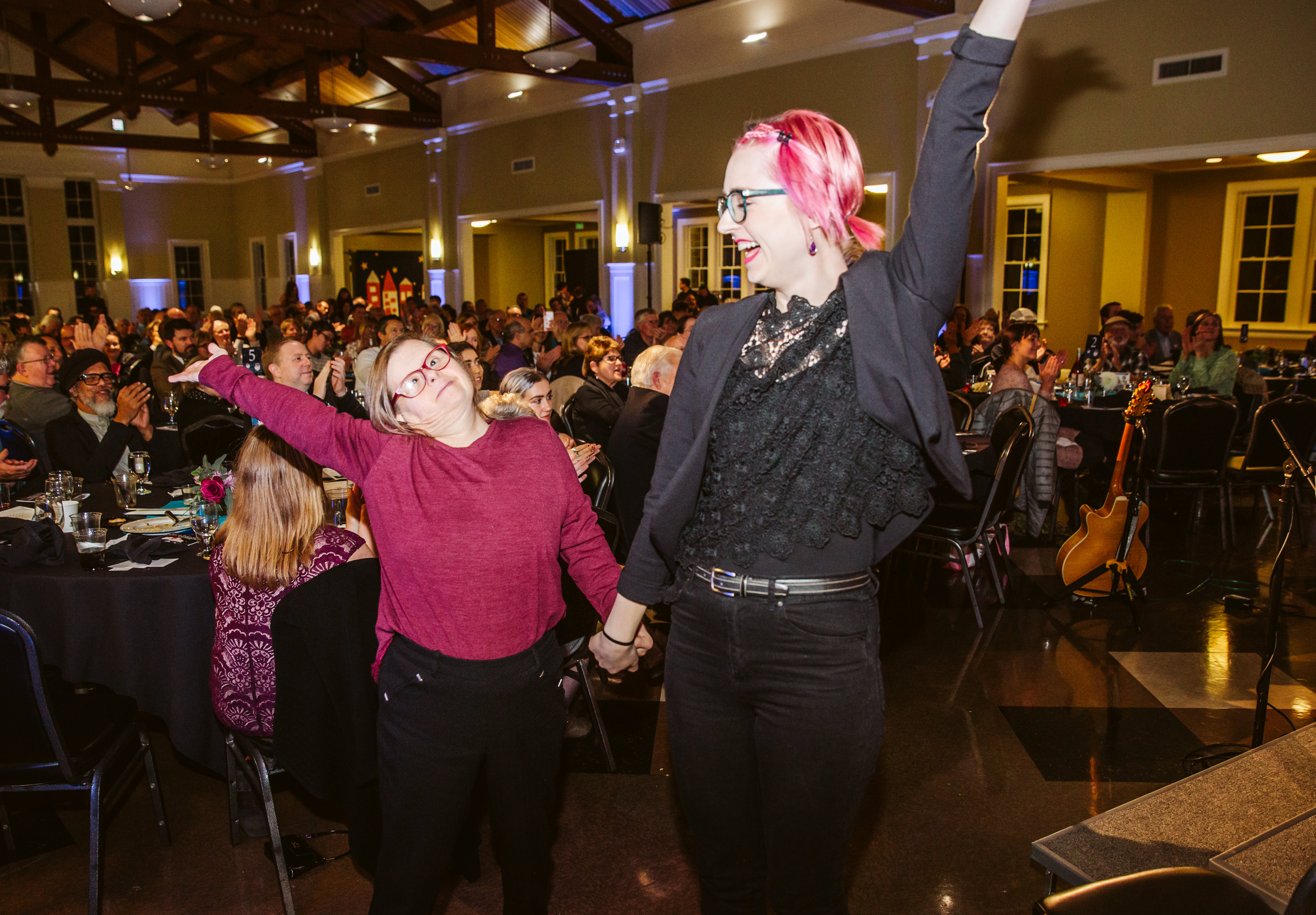 Two women dancing and smiling at a community event in a large hall.
