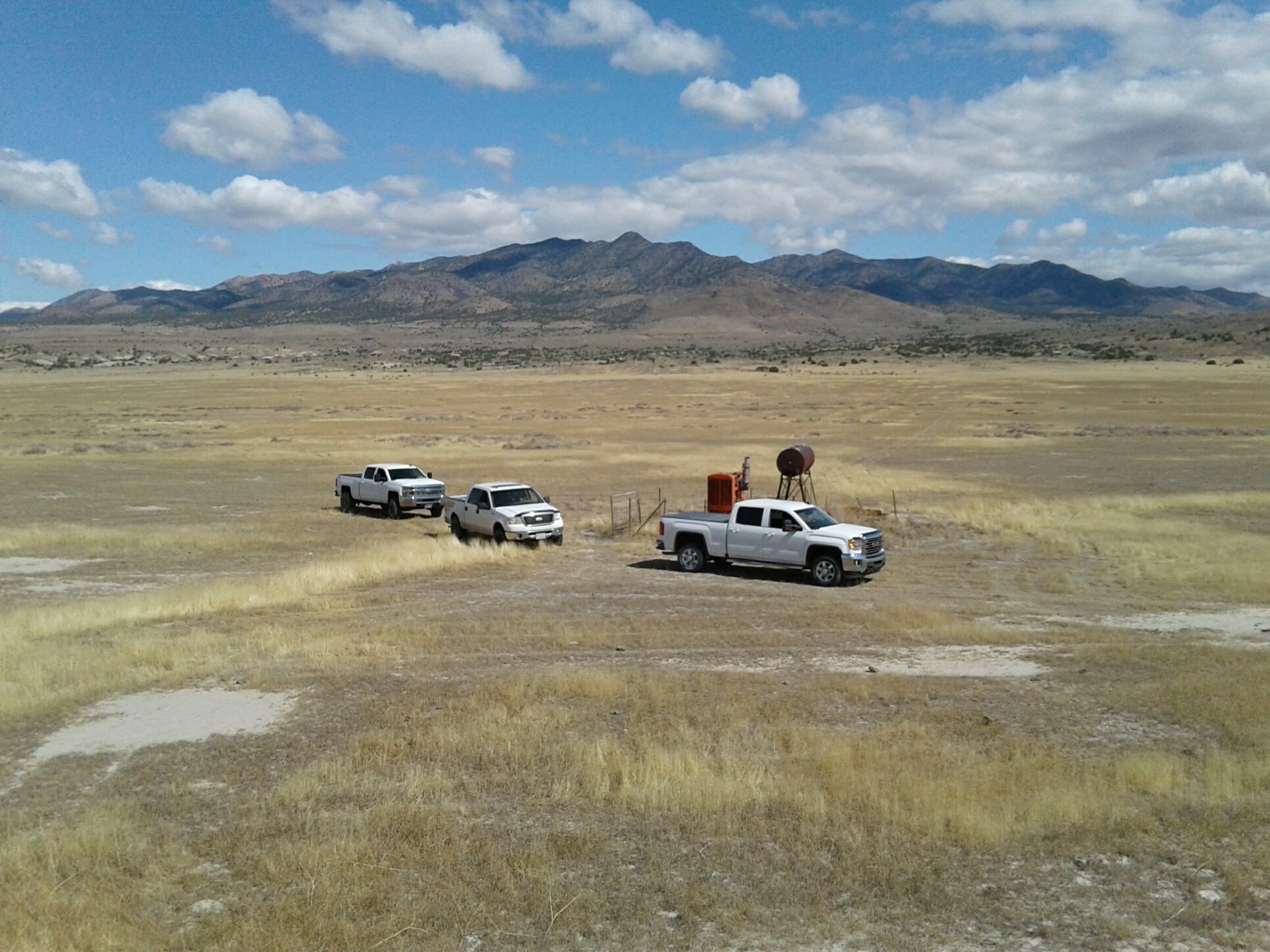 Vehicles parked on open land with mountains in the background.