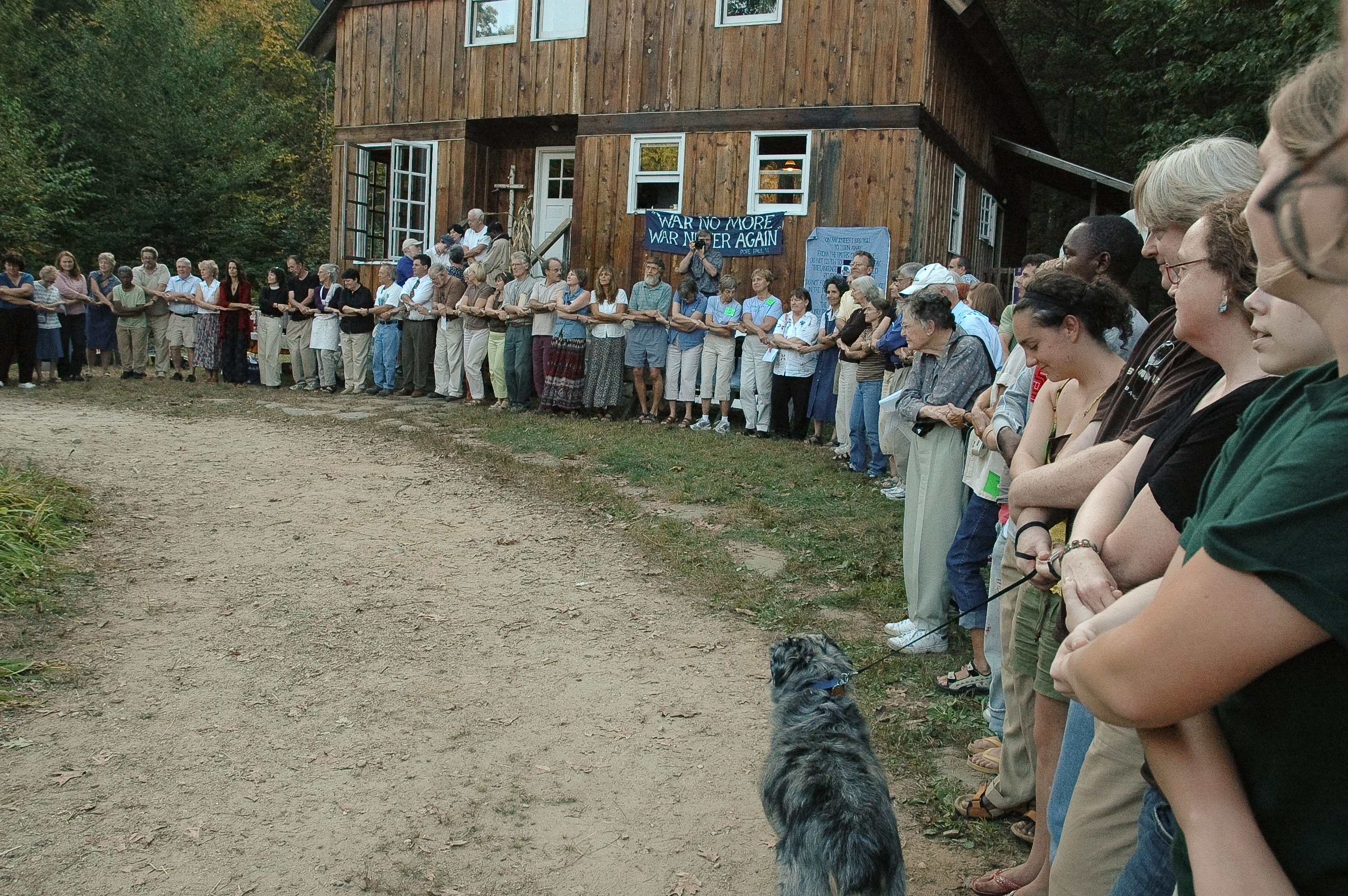 People gathered in a circle outside a wooden building for community event.