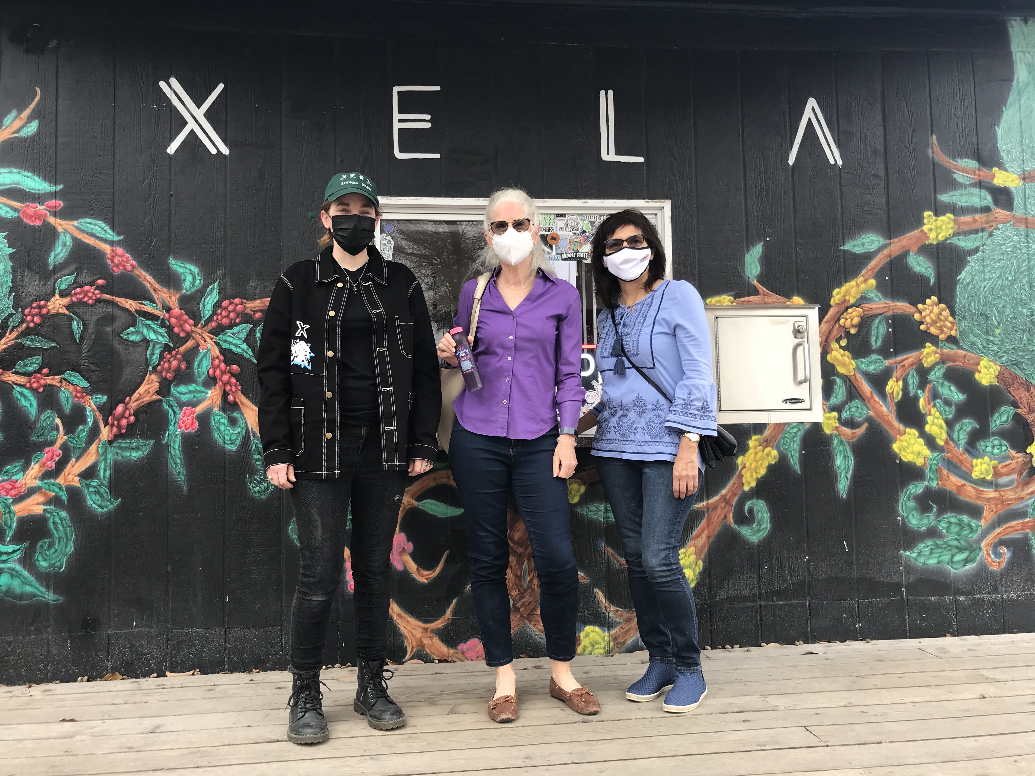 Group of three diverse people wearing masks in front of XELA mural.