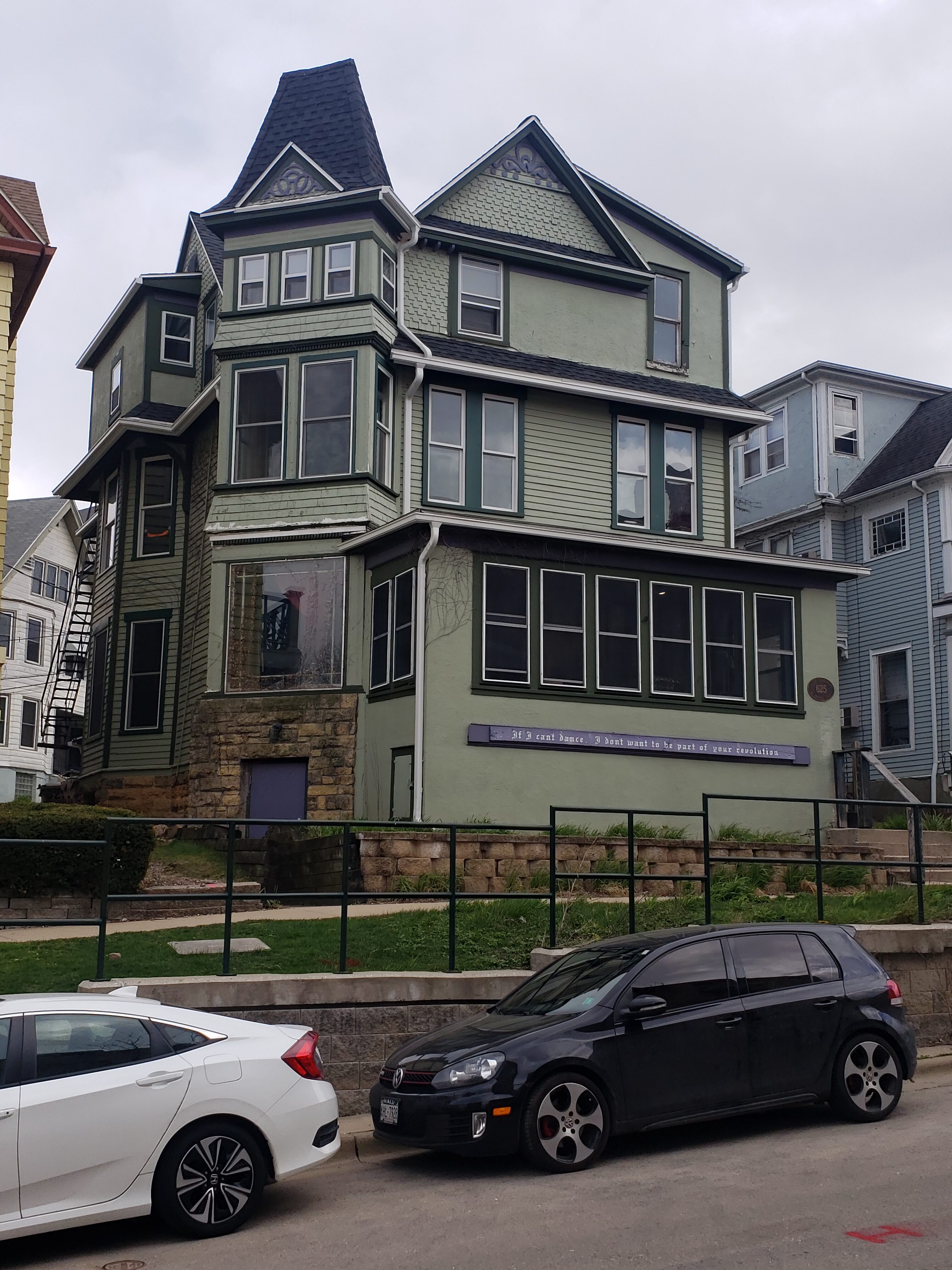 Victorian house with green siding and multiple bay windows in an urban neighborhood.