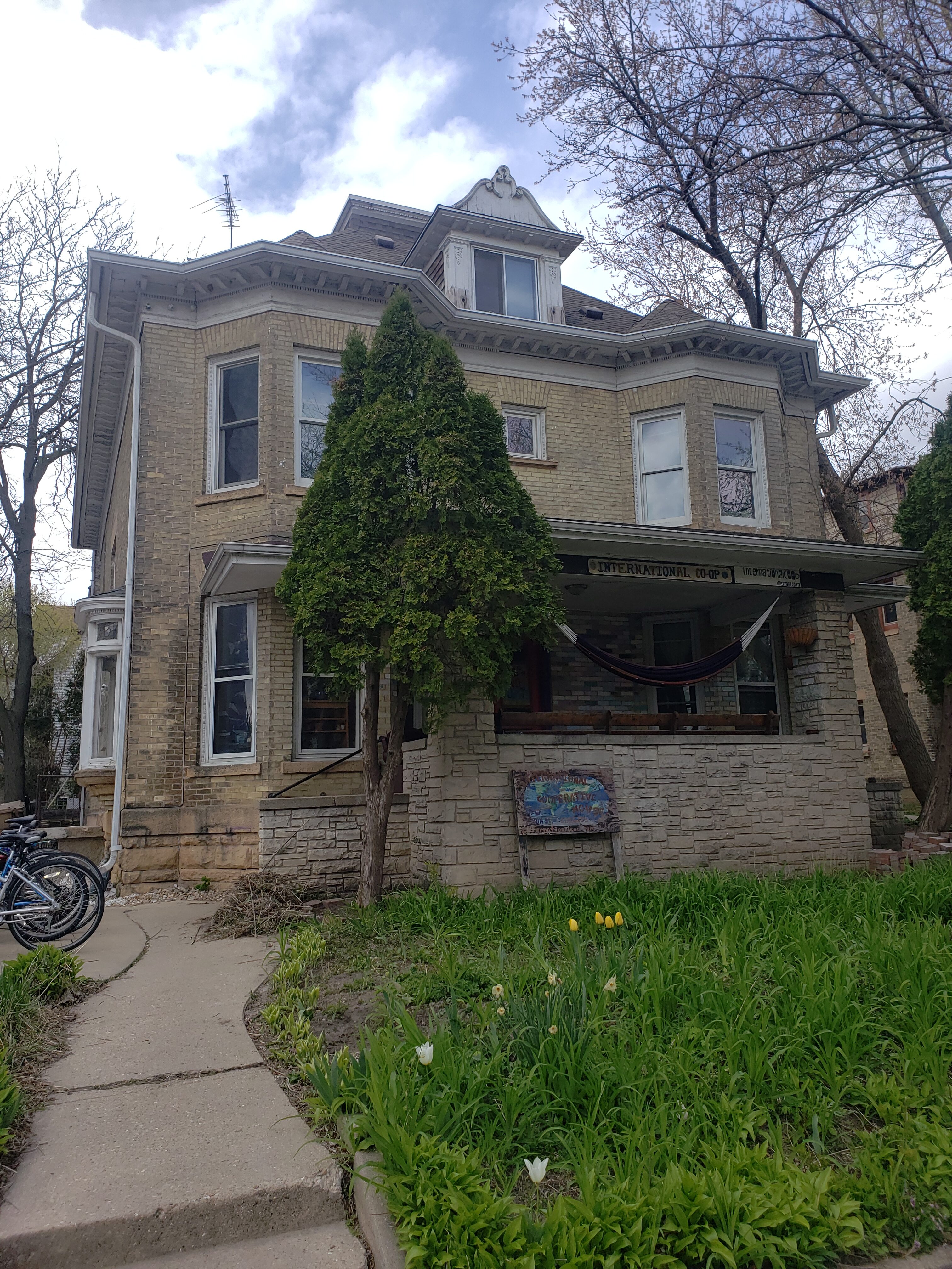 Victorian house with lush greenery and a hammock in front yard.