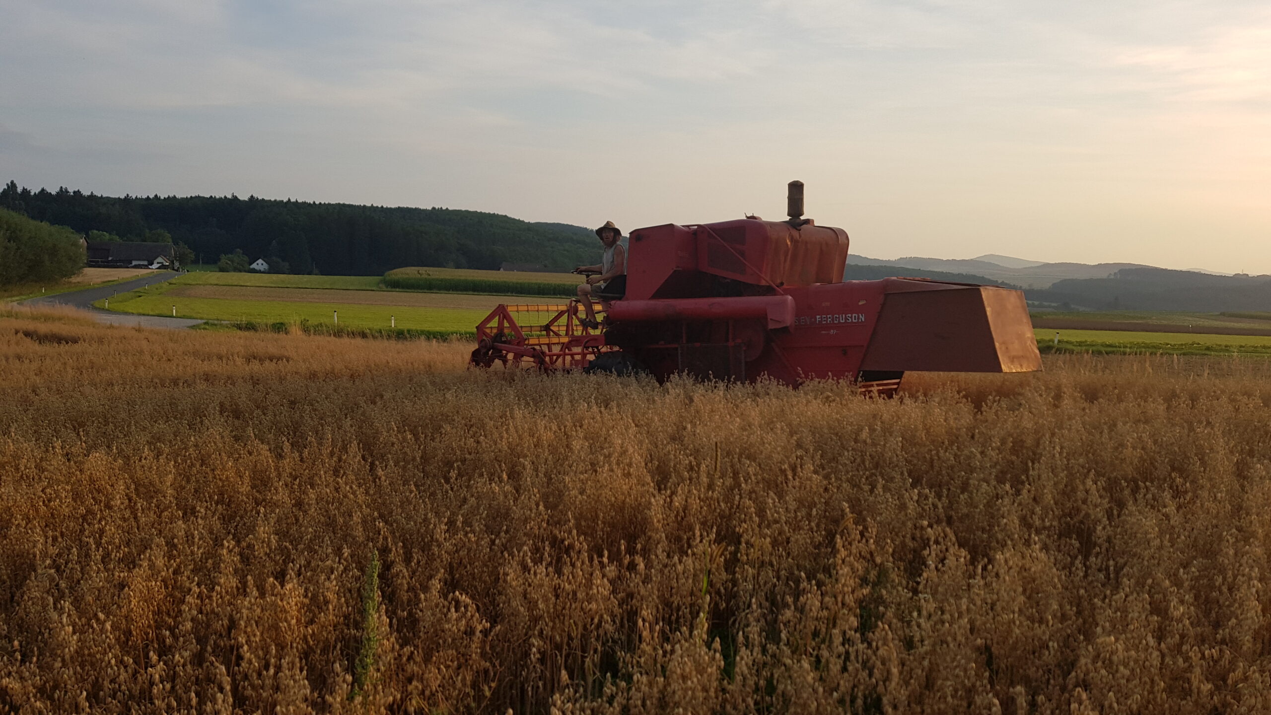 Red farm machinery in a field during sunset with rolling hills in the background.