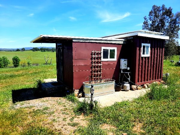 Small red cabin with white window in green field under blue sky.