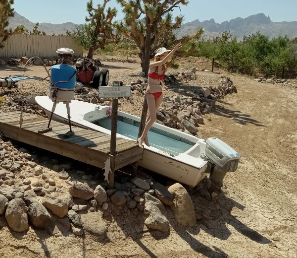 Person in swimsuit standing on small boat in desert landscape with mountains.