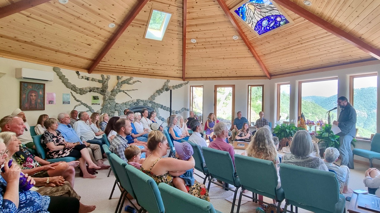 People attending a community meeting in a wooden dome with large windows.