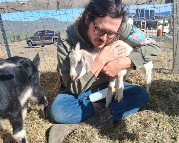 Person holding a baby goat at Companion Ranch for community living.