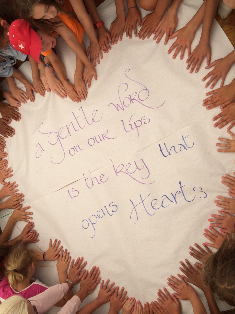Group of diverse children with hands around a message about kindness and hearts.