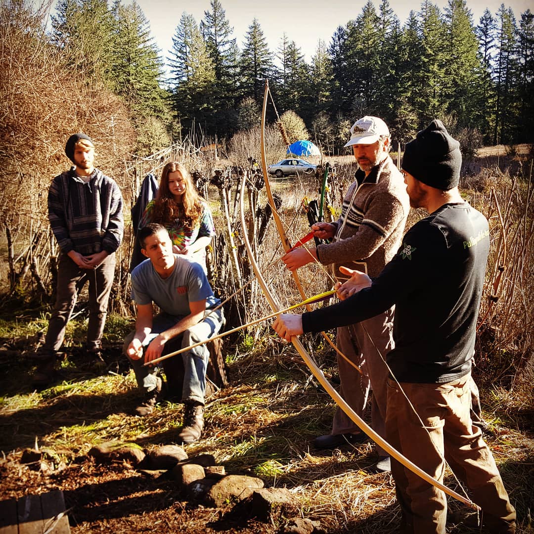 Group of people practicing archery outdoors in a forested area.