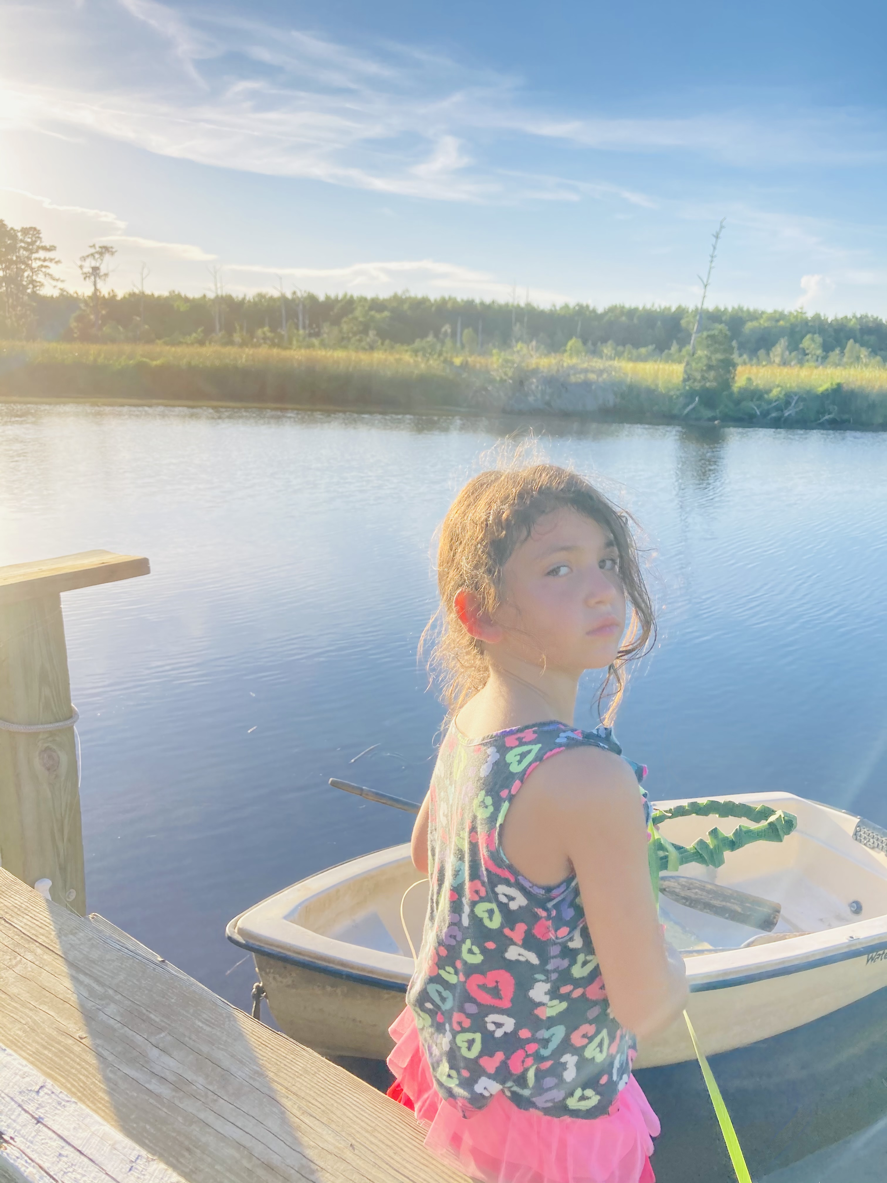 Young girl by a boat on a peaceful river at sunset.