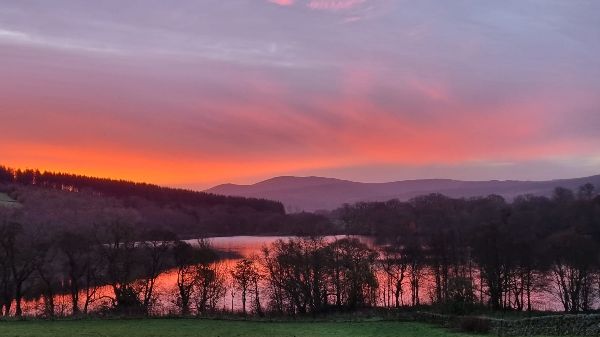 Beautiful sunset over a lake with trees and mountains in the background.